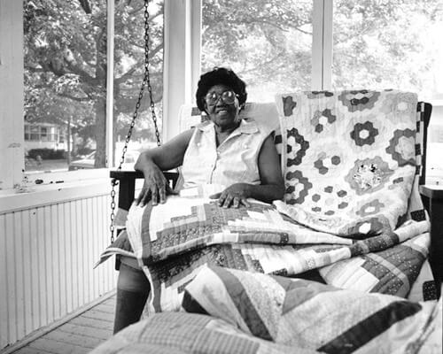 Black and White Photo of Rosie Lee Wilkins with her quilts.